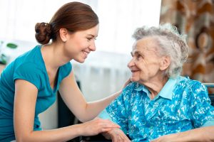 young woman providing respite care smiling at elderly woman